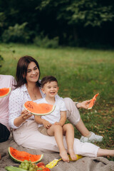 outdoor group portrait of happy family having picnic on green grass in park. father is cutting watermelon.