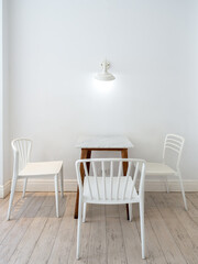 Vintage light lamps hanging on white wall over the empty dining table set with marble top table with wood legs and three chairs, minimal style living room. Bright cafe or restaurant interior decor.