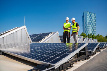 Two technicians utilizing a tablet PC while working on the rooftop of a corporate building equipped with solar panels