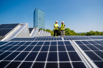 Two technicians utilizing a tablet PC while inspecting solar panels on the rooftop of a corporate building