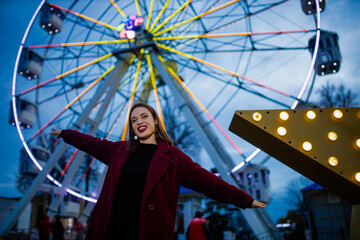 beautiful woman in burgundy coat in amusement park in winter evening
