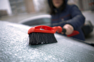 A girl with a special brush cleans the car window from snow