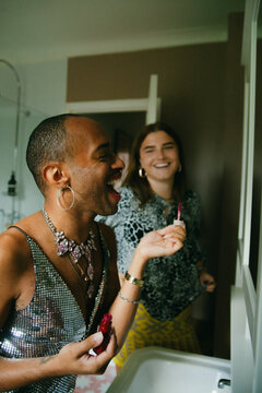 Young non-binary person of Caribbean mixed race laughing with their white female friend while applying lipstick