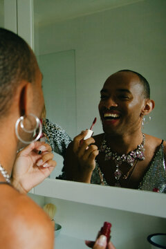 Young non-binary person of Caribbean mixed race laughing happily applying lipstick in the bathroom