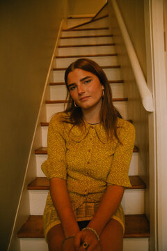 Young white woman posing in fashionable outfit on stairs at home