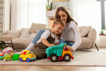 young mother plays with her little son with toys at home and smiles, 2-year-old boy plays with toy car with his parent - obrazy, fototapety, plakaty