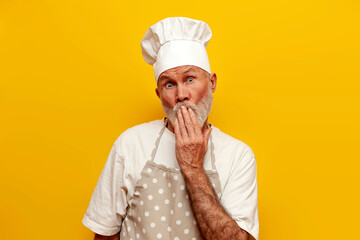 shocked old grandfather chef in apron and hat is surprised and covers his mouth with his hand