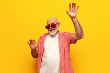Photo sur Plexiglas Vielles portes pensioner old grandfather in sunglasses dances and sings to music at party on yellow isolated background