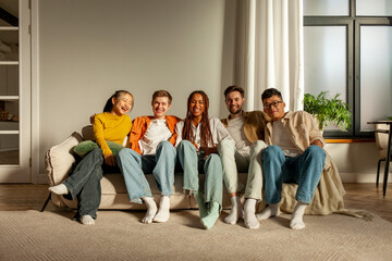 Fototapeta premium multiracial group of young friends sitting on sofa at home hugging and looking at camera