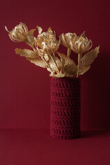 Flowers made of straw on a red background in a knitted vase