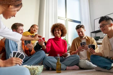 Fotobehang multiracial group of young friends playing cards drinking beer and having fun at home, students sitting on the floor © Богдан Маліцький