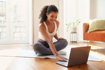 Happy young lady using laptop for online yoga class indoors