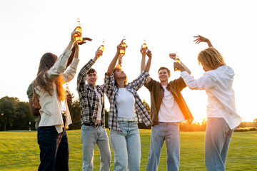 group of young multiracial students holding beer bottles and dancing at outdoor party, interracial people relaxing
