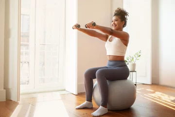 Foto op Plexiglas lady performs arm workout holding dumbbells using balance ball indoor © Prostock-studio
