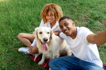 african american young couple sit in park together with dog and take selfie, man and woman with retriever