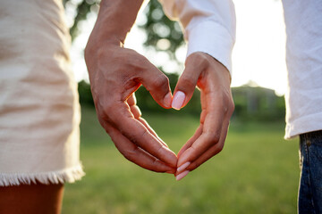 heart shaped hands of young african american couple in park outdoors at sunset, closeup of hands of...