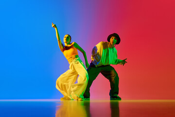 Stylish, young, active and talented boy and girl in modern clothes dancing hip-hop against blue red...