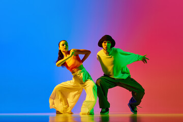 Street style dance. Young people, artistic man and woman in motion, performing hip hop against blue red background in neon. Concept of hobby, action, street style, contemporary dance, youth, fashion