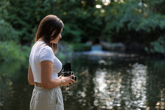 Young woman with vintage camera by pond - Powered by Adobe