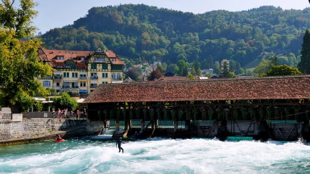 Man Surfer Riding the Wave on River Aare with an Old Bridge Obere Schleuse in City of Thun in a Sunny Summer Day in Thun, Bernese Oberland, Bern Canton, Switzerland.