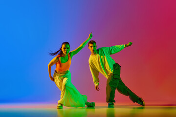 Coordinated movements. Young man and woman, street dancers in motion, dancing hip hop against blue red background in neon. Concept of hobby, action, street style, contemporary dance, youth, fashion