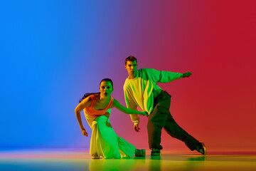 Coordinated movements. Young man and woman, street dancers in motion, dancing hip hop against blue...