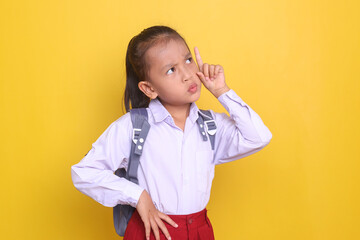 Smart Asian little girl wearing school uniform and carrying backpack looking up showing confused or...