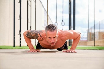 Man doing push up and looking at camera in an outdoor training gym. Cross Fit, fitness and sport.