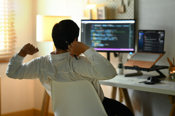 Back view of male programmer stretching arms and relaxing on chair at his workplace
