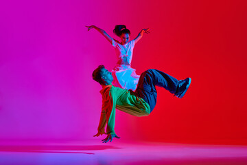 Expressive performance. Young man and woman, talented dancers in motion, dancing hip hop against pink red background in neon. Concept of hobby, action, street style, contemporary dance, youth, fashion