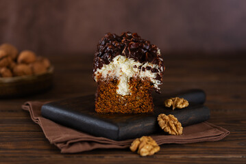 Carrot cake with vanilla cream cheese, chocolate and walnuts on a wooden board.