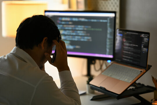 Overworked male programmer feeling frustrated and tired while working on computer code at night
