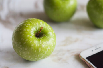 Green apples lie on a marble table. There is a telephone nearby