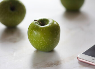 Green apples lie on a marble table. There is a telephone nearby