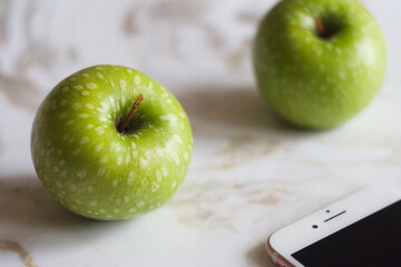 Green apples lie on a marble table. There is a telephone nearby