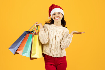 woman in Santa hat holds shopping bags against yellow backdrop