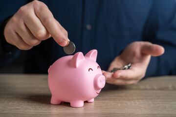 A man puts coins in a piggy bank. Accumulating money. Savings and investments. Collection of donations. Bank deposit. Raise funds for your dream. Reduce costs. Save for retirement.