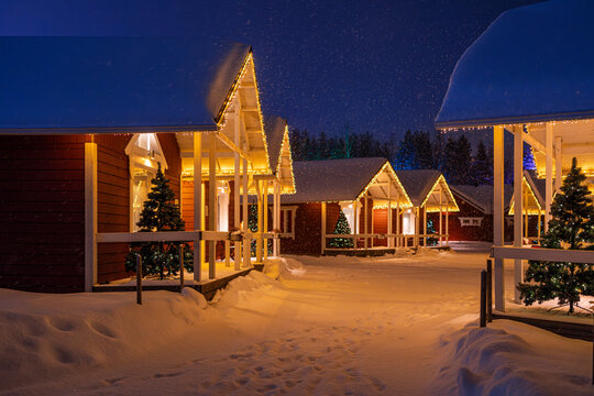 A serene winter night scene in Rovaniemi Finalnd featuring cozy cottages adorned with festive lights amidst a tranquil snowfall - Powered by Adobe