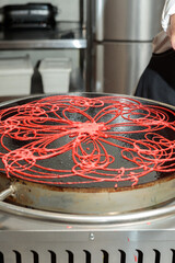 Baking colored Asian pancakes. The red dough is poured on the baking surface.