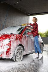 Woman in red checkered shirt washing the car and looking busy