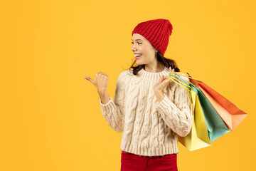 woman with shopping bags in sweater points aside, yellow background