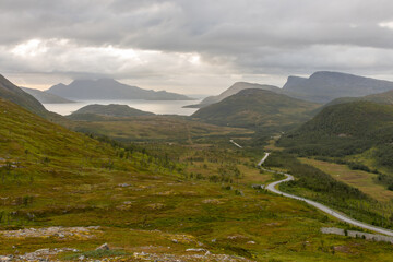 Winding road between green meadow and lake on the horizon