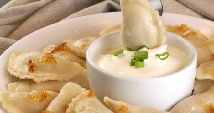 Dumplings with fried onions and bowl with sour cream. Varenyky, vareniki, pierogi, pyrohy with filling.
Close-up footage on the rotating table.Takes dumplings with a fork.