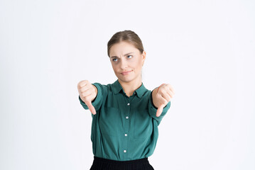 Attractive young woman shows a thumbs down. The girl has negative emotions, shows dislike, disagreement, distrust, isolated on a white studio background