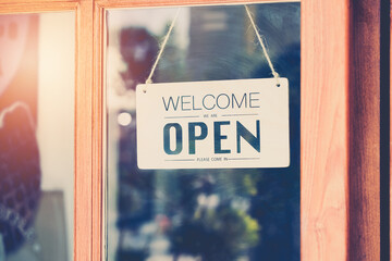 Welcome we're open word on wooden signboard behind transparent mirror door , vintage retro sign in front of cafe or restaurant - obrazy, fototapety, plakaty
