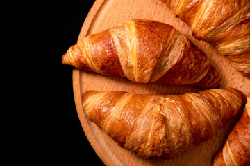 Fresh croissants on a wooden board on a black background. French pastries, top view
