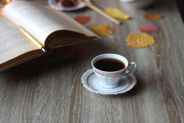 Cup of tea or coffee, plate with desserts, dried oranges, bowl of grapes, scented candles, vintage books, pumpkins and autumn leaves on the table. Autumnal hygge. Selective focus.