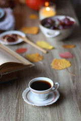 Cup of tea or coffee, plate with desserts, dried oranges, bowl of grapes, scented candles, vintage books, pumpkins and autumn leaves on the table. Autumnal hygge. Selective focus.