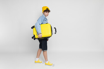 Curly teenager boy with a suitcase on a gray background.