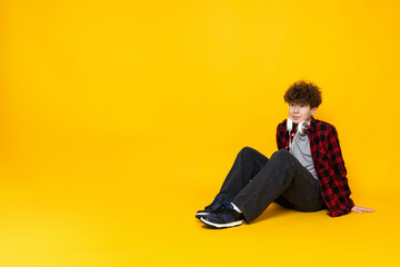 Curly boy teenager sitting on the floor, on a yellow background.